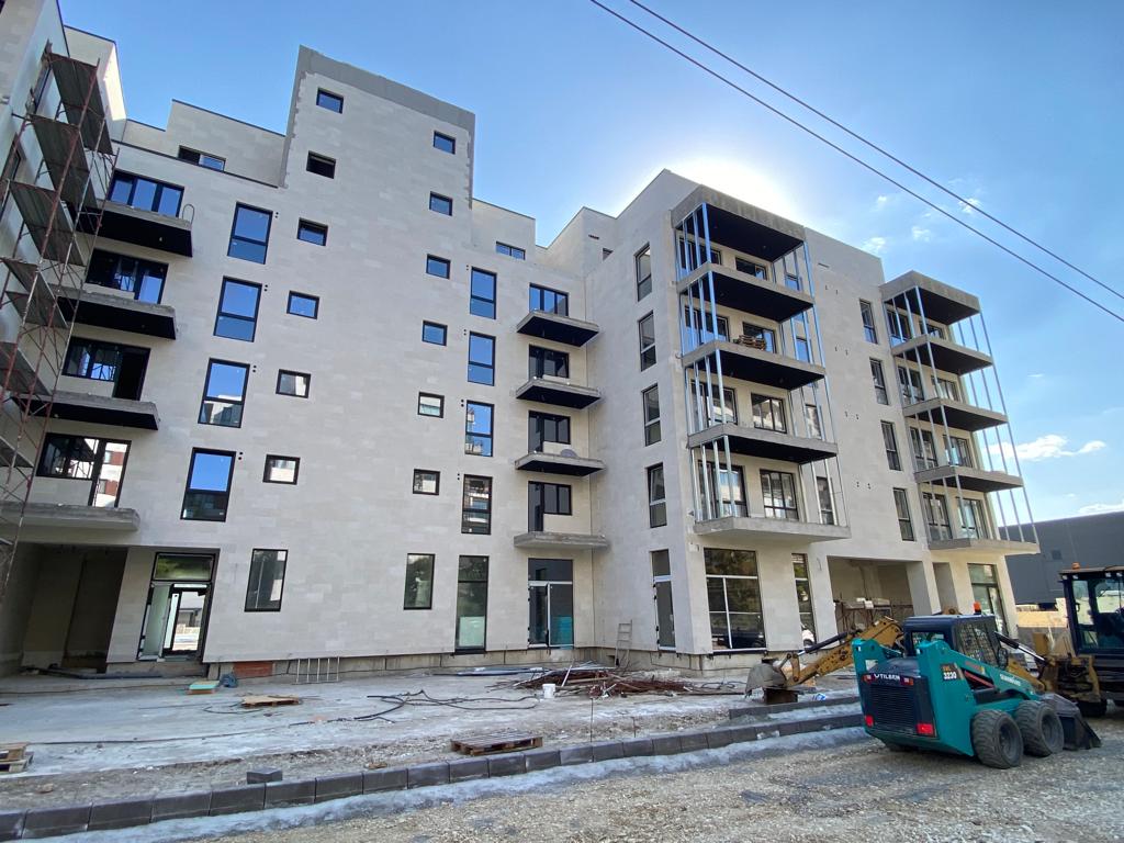 Bloc cu balcoane în contralumină, placat cu piatră flexibilă bej, cu un excavator pe pietriș