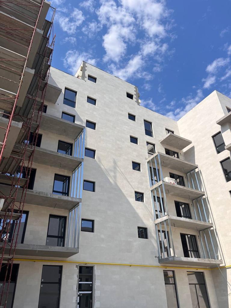 Bloc contemporan văzut de jos, cu schele cu balustrade roșii și balcoane în consolă din piatră bej