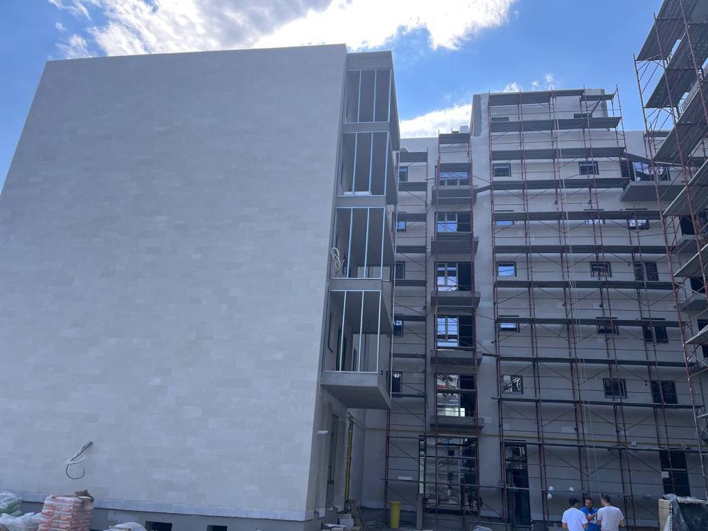 Calcan bej fotografiat de jos, cu un bloc pe schele și muncitori în plan secund