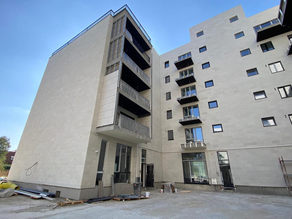 Bloc cu turn de scară placat în antracit și balcoane bej, pe un teren de șantier