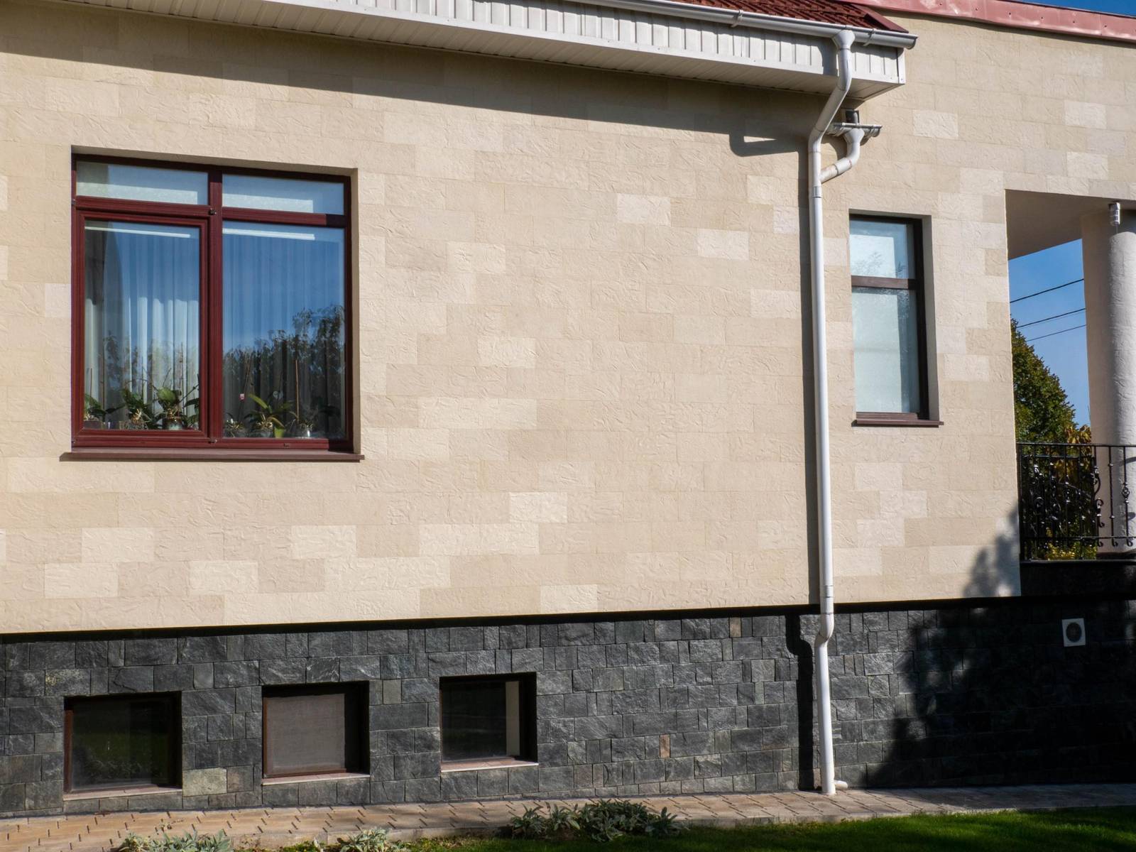 Colțul casei cu fereastră, burlan alb și piatră flexibilă Tender Rock, văzut de jos