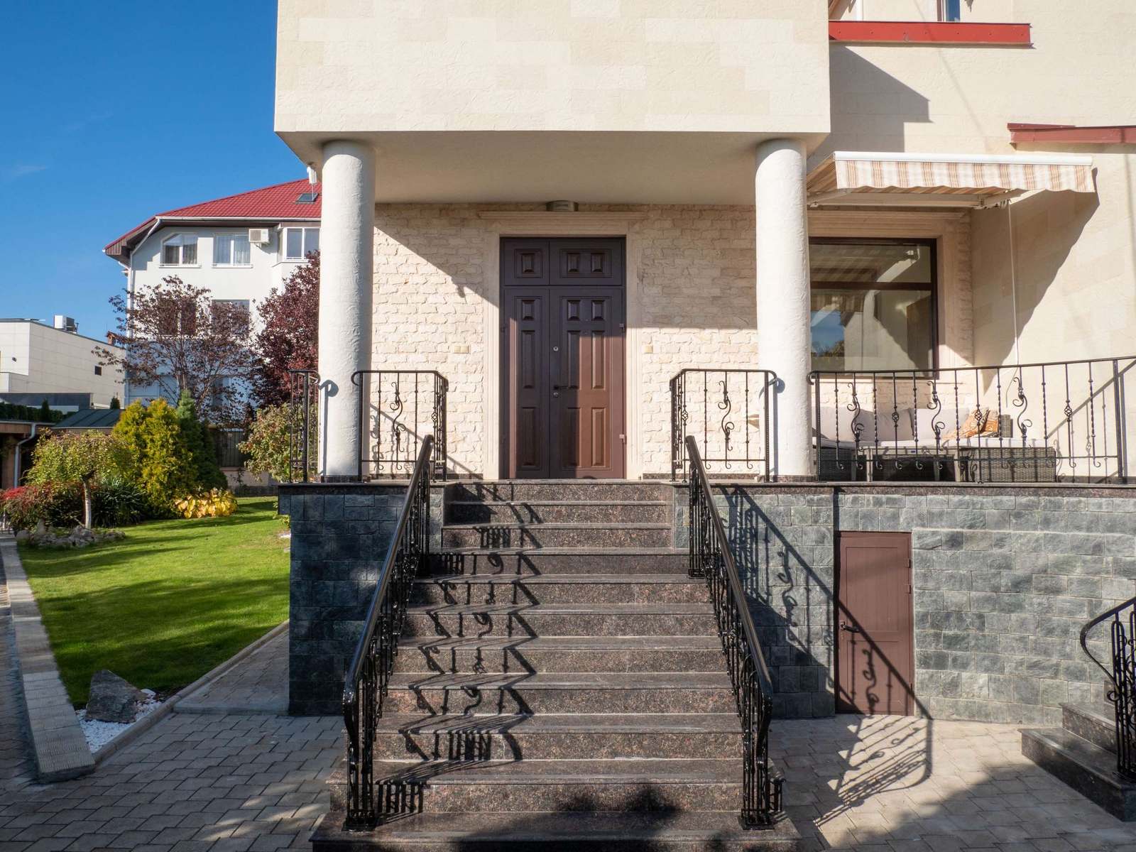Intrarea principală cu trepte, balustrade forjate și două coloane rotunde placate cu piatră flexibilă