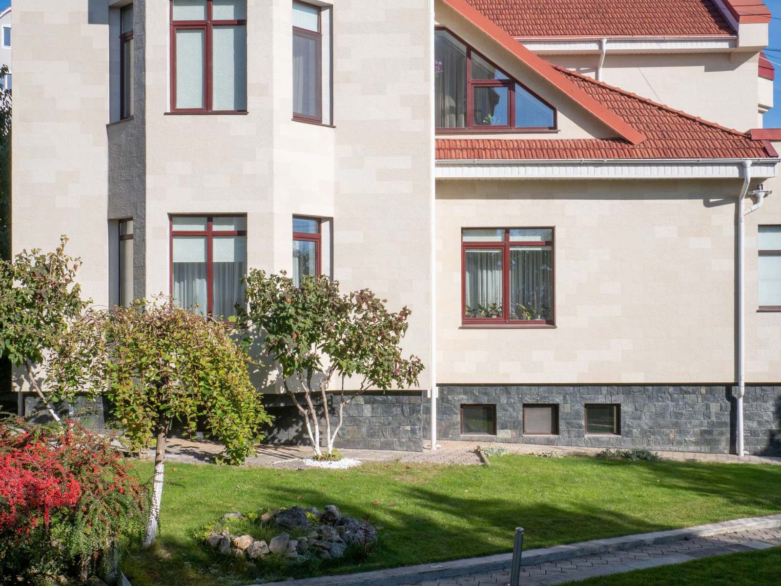 Latura casei cu ferestre cu rame maro și fațadă din piatră flexibilă Tender Rock, arbuști în față