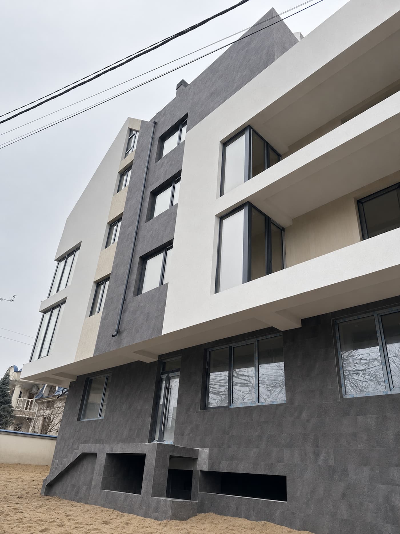 Fațadă cu volume albe și placare Royal Granite pe parter și pe banda verticală, vedere de jos