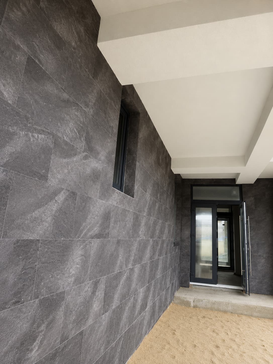Intrarea sub consola albă: perete placat Royal Granite, fereastră îngustă și ușă din sticlă