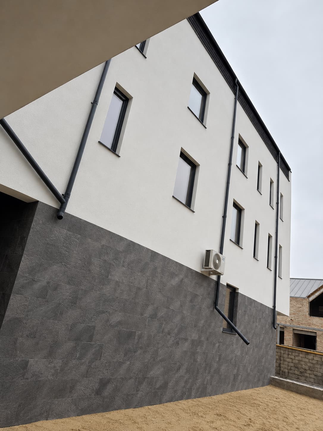 Fațada laterală: soclu înalt placat Royal Granite sub peretele alb cu ferestre mici