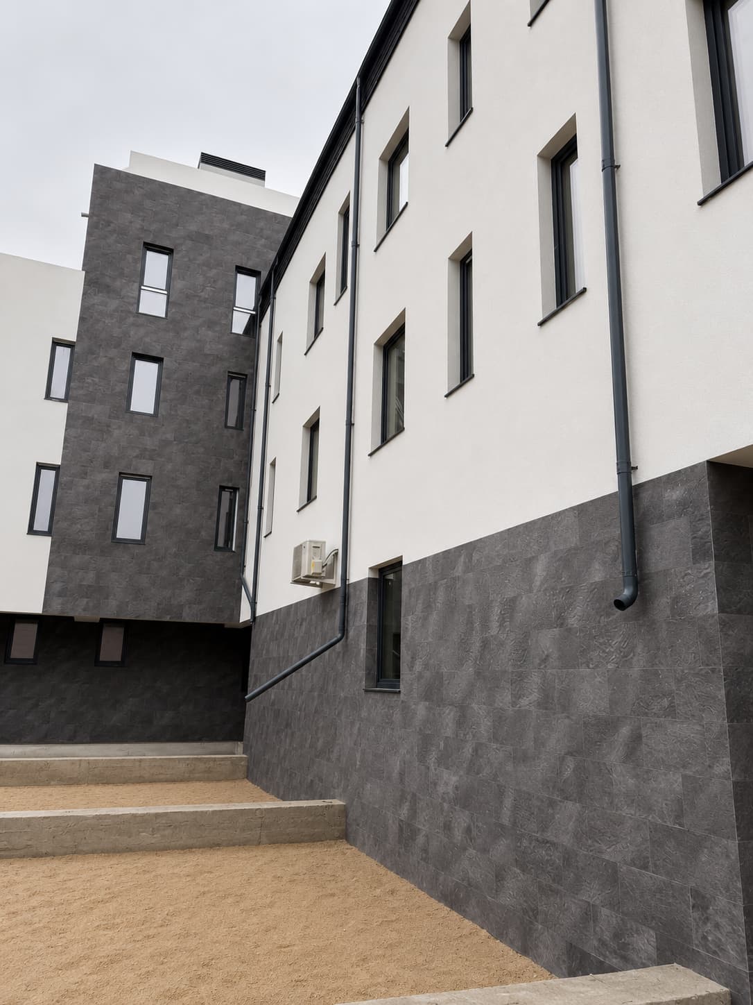Curtea interioară: volum placat integral Royal Granite lângă aripa albă cu soclu din piatră flexibilă