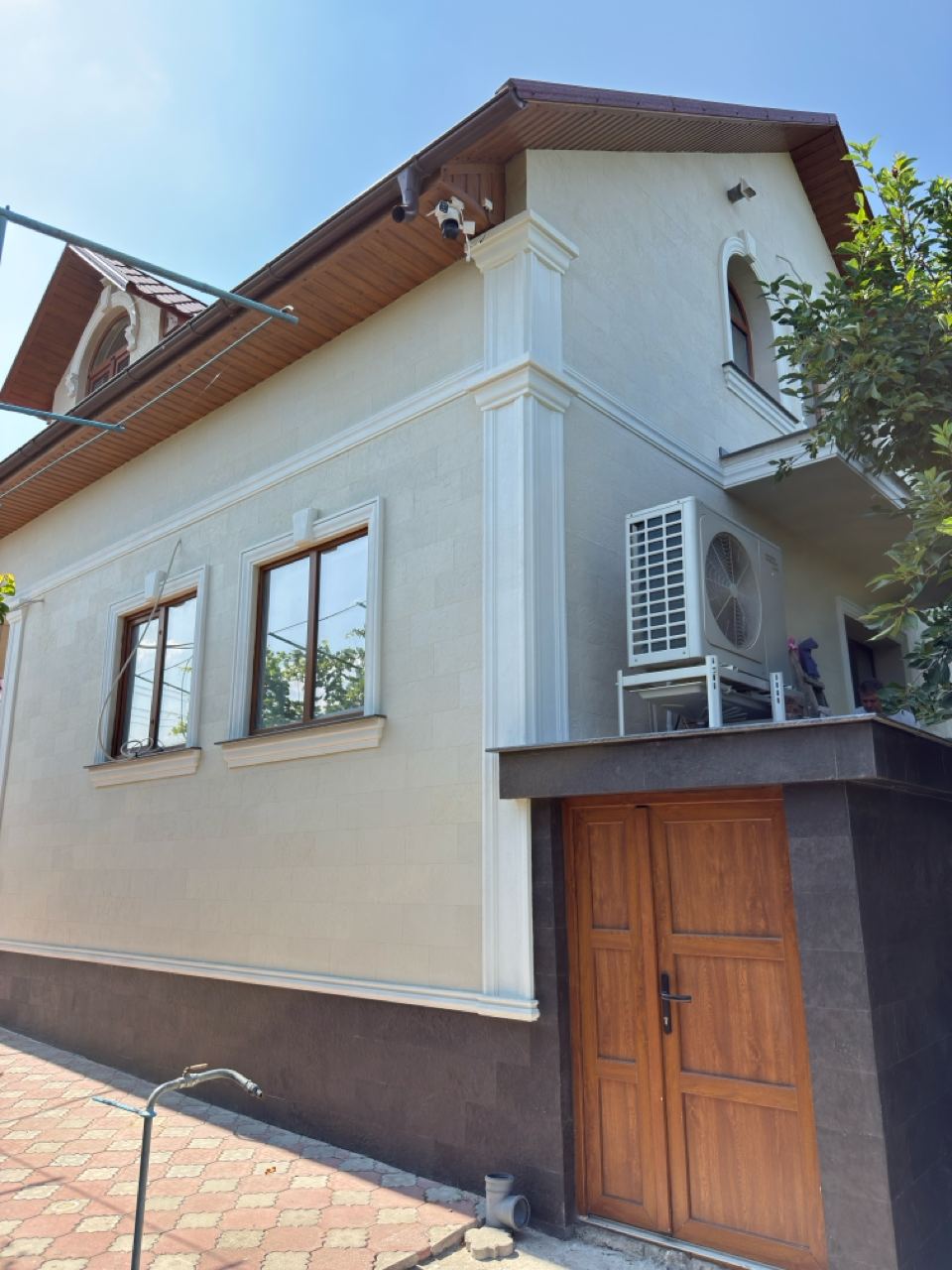 Colțul casei cu piatră flexibilă deschisă, cornișă albă, două ferestre și ușă de lemn, soclu închis