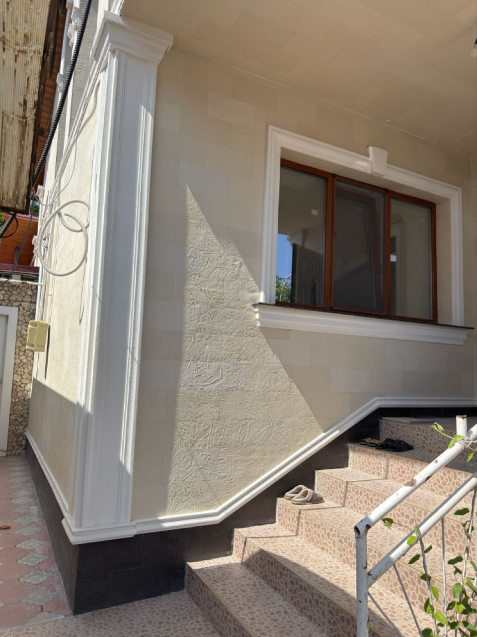 Fereastră cu ancadrament alb lângă scara de acces, perete din piatră flexibilă deschisă și soclu închis