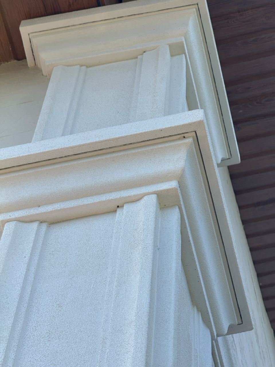 Capitel de pilastru alb peste peretele placat cu piatră flexibilă deschisă