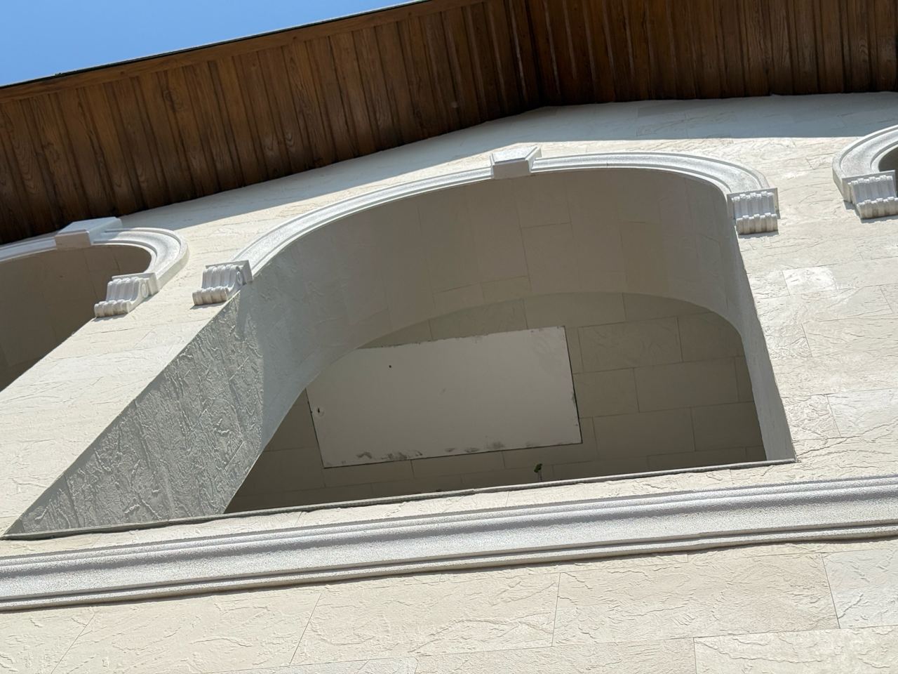 Balcon arcuit cu bosaje albe pe fațada placată cu piatră flexibilă deschisă