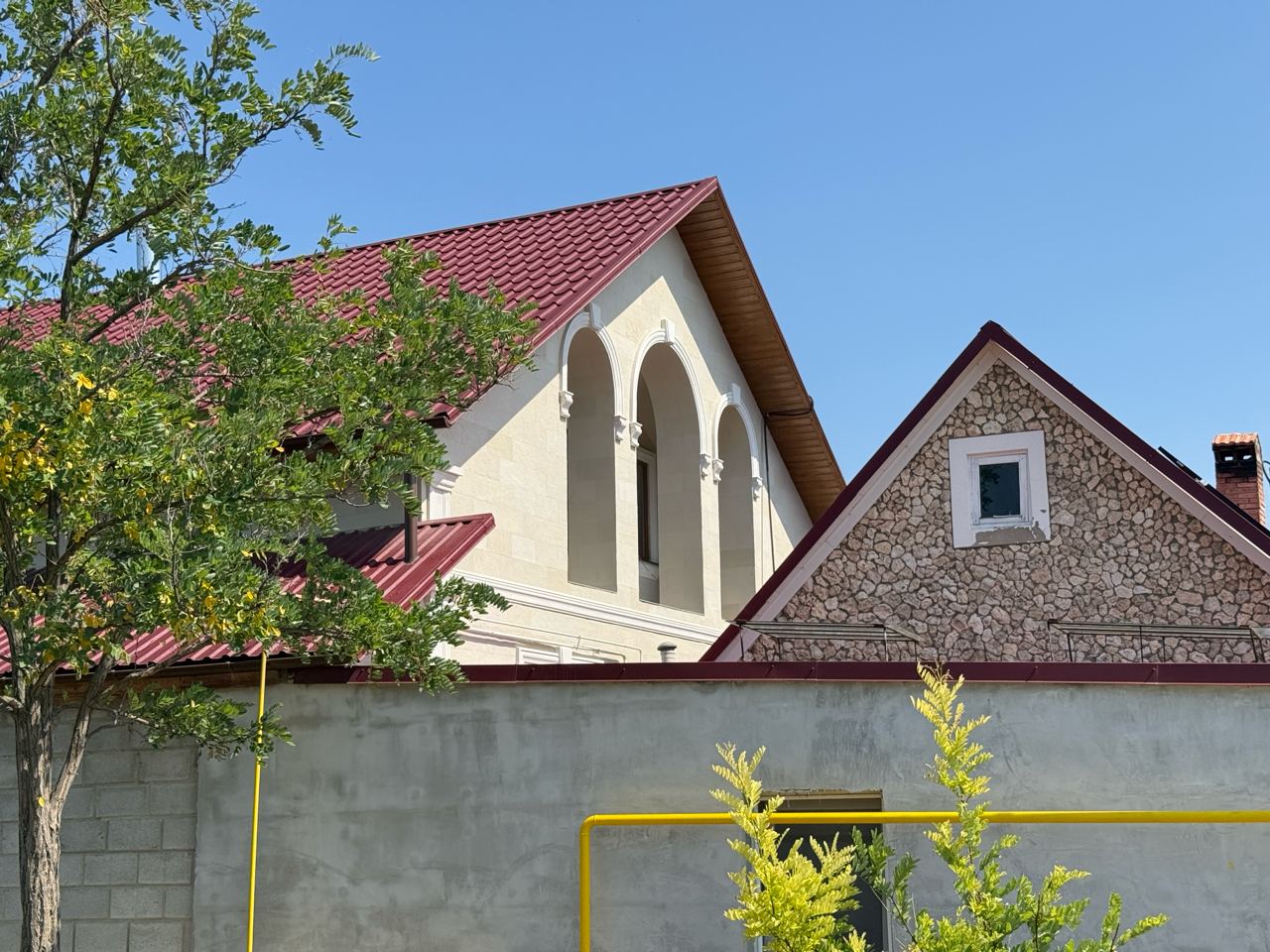 Casă crem placată cu piatră flexibilă deschisă, arcade cu ancadramente albe și acoperiș de țiglă