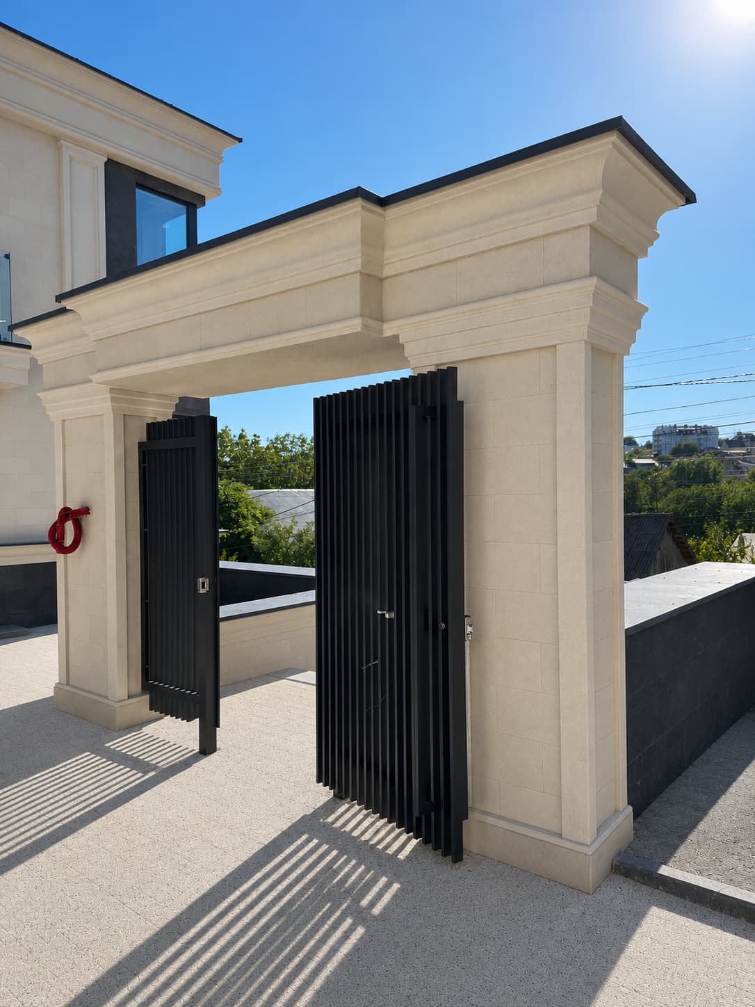 Arcada de intrare văzută din curte: doi pilaștri și un buiandrug din piatră flexibilă bej, poartă neagră