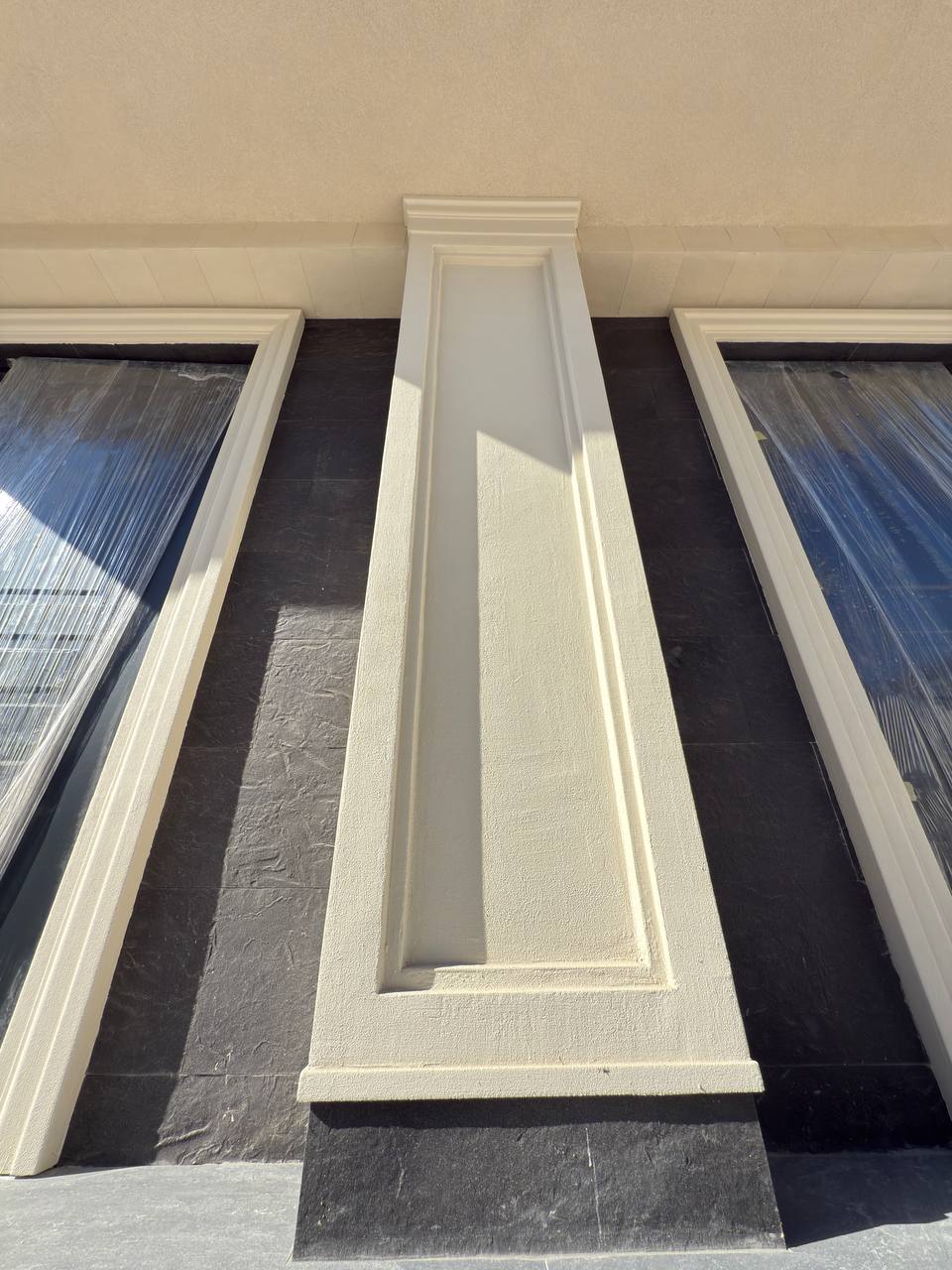Pilastru canelat bej pe un panou vertical antracit, între două ferestre, văzut de jos