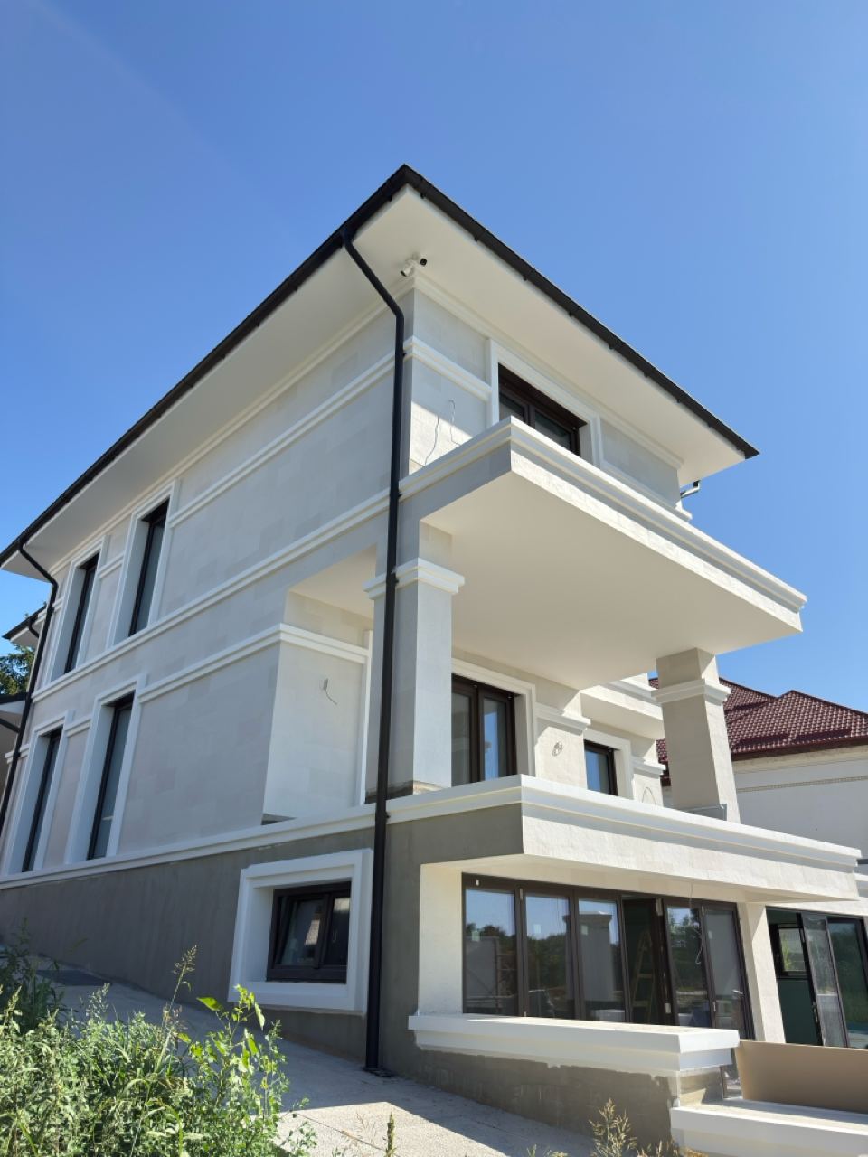 Casa întreagă văzută din stradă, trei niveluri placate cu piatră flexibilă albă și cornișe albe, plante în față