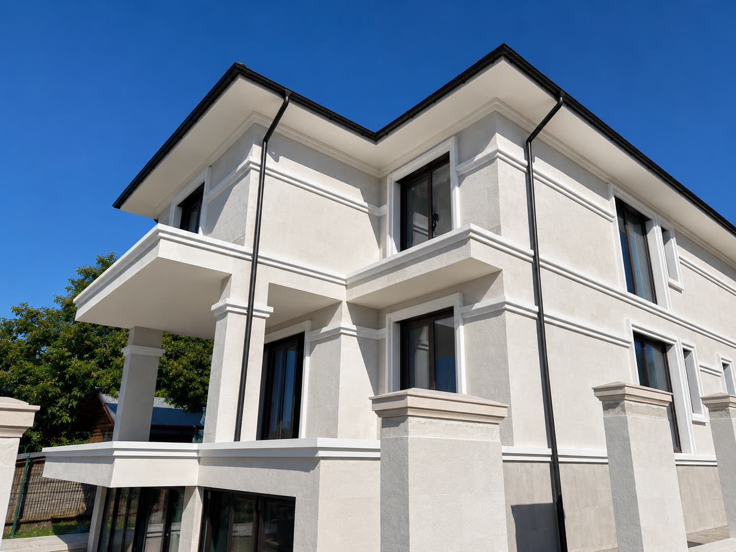 Casă pe trei niveluri văzută de jos: piatră flexibilă Mont Blanc între cornișele albe, balcon și cer senin