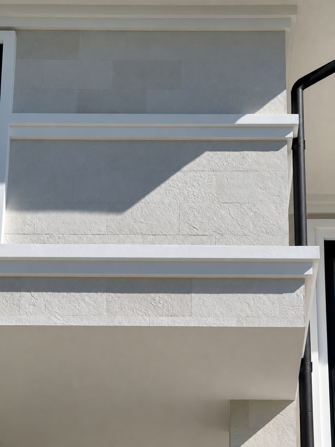 Parapet de balcon și colț superior placate cu piatră flexibilă albă, sub o bandă albă